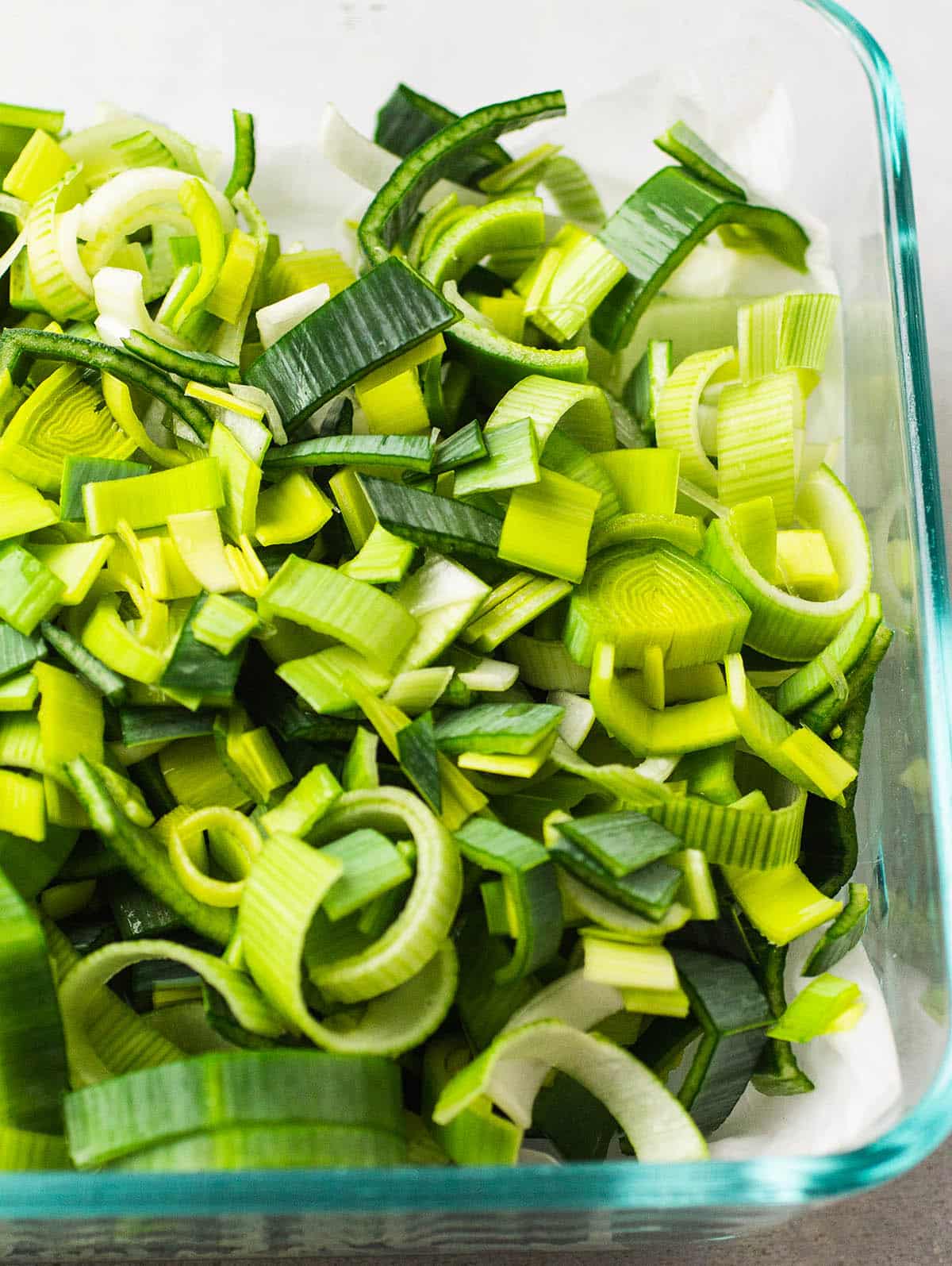 Sliced leeks in a glass container lined with a paper towel.