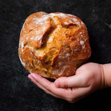 Hand holding a small loaf of bread in front of a black background.