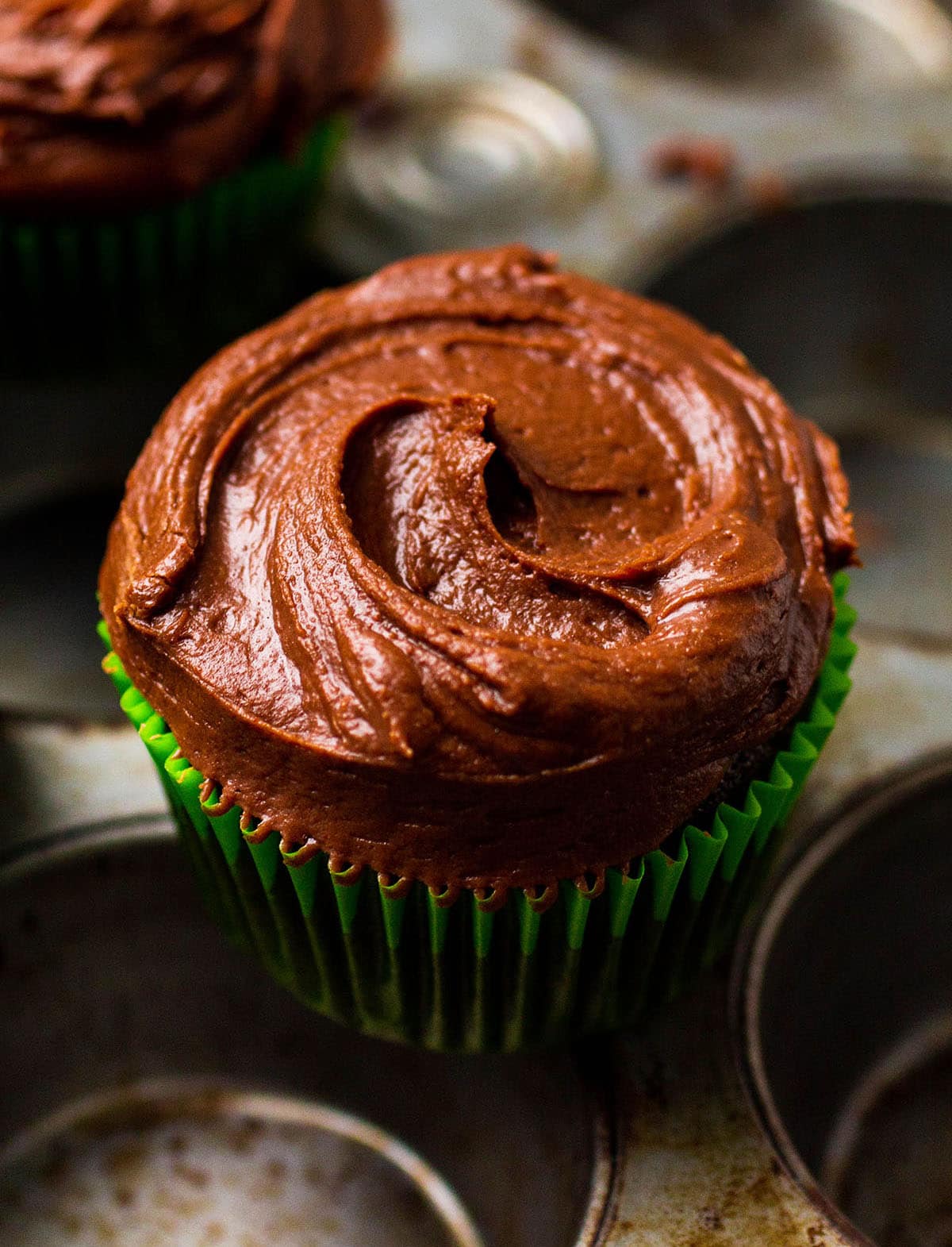 Chocolate cupcake in a green wrapper on top of a metal pan.
