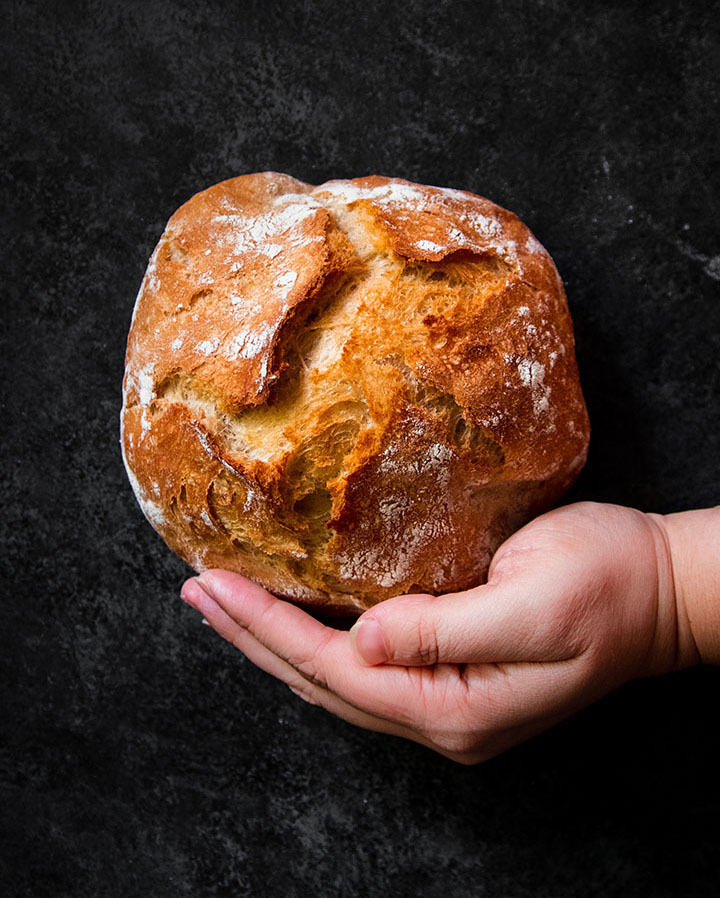 Hand holding a small loaf of bread in front of a dark background.