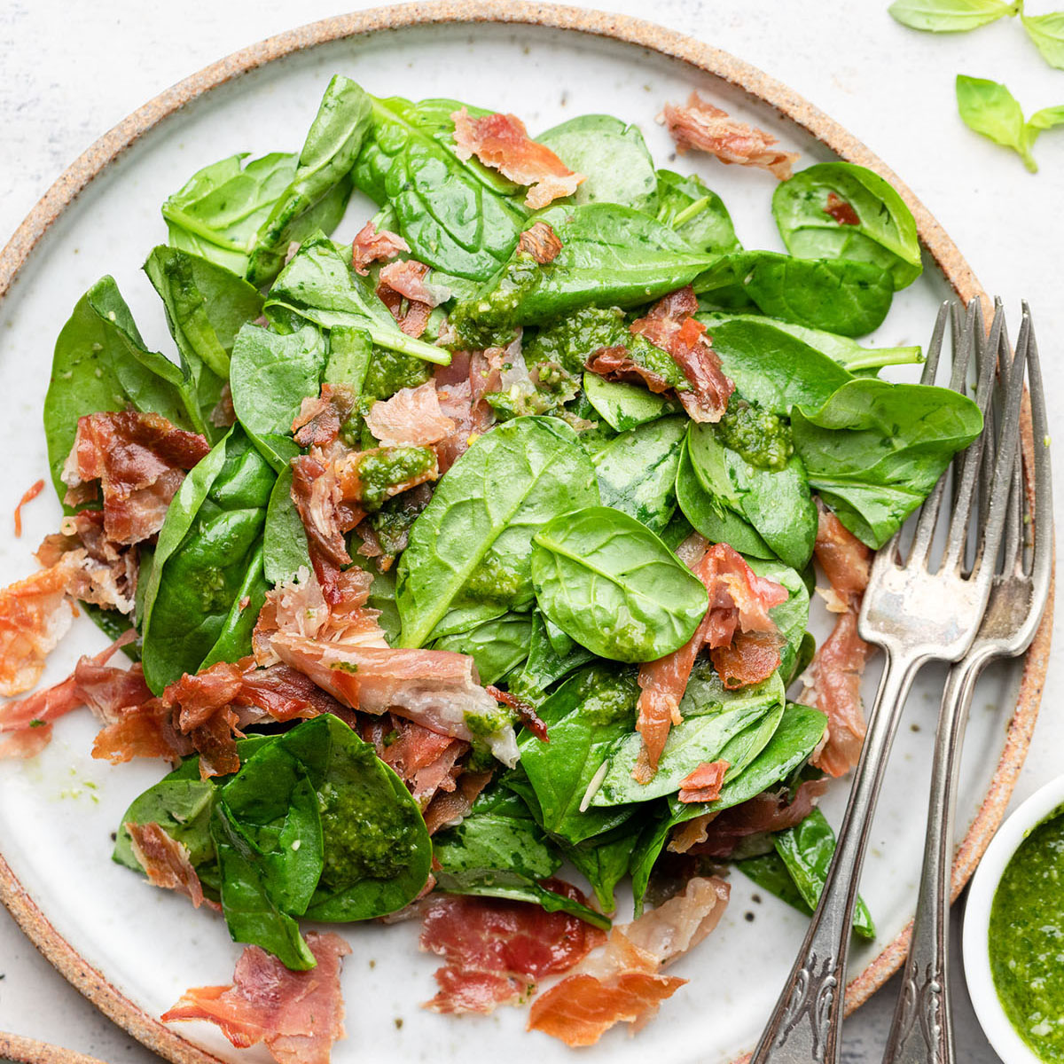 Spinach salad on a white plate, topped with crispy prosciutto.