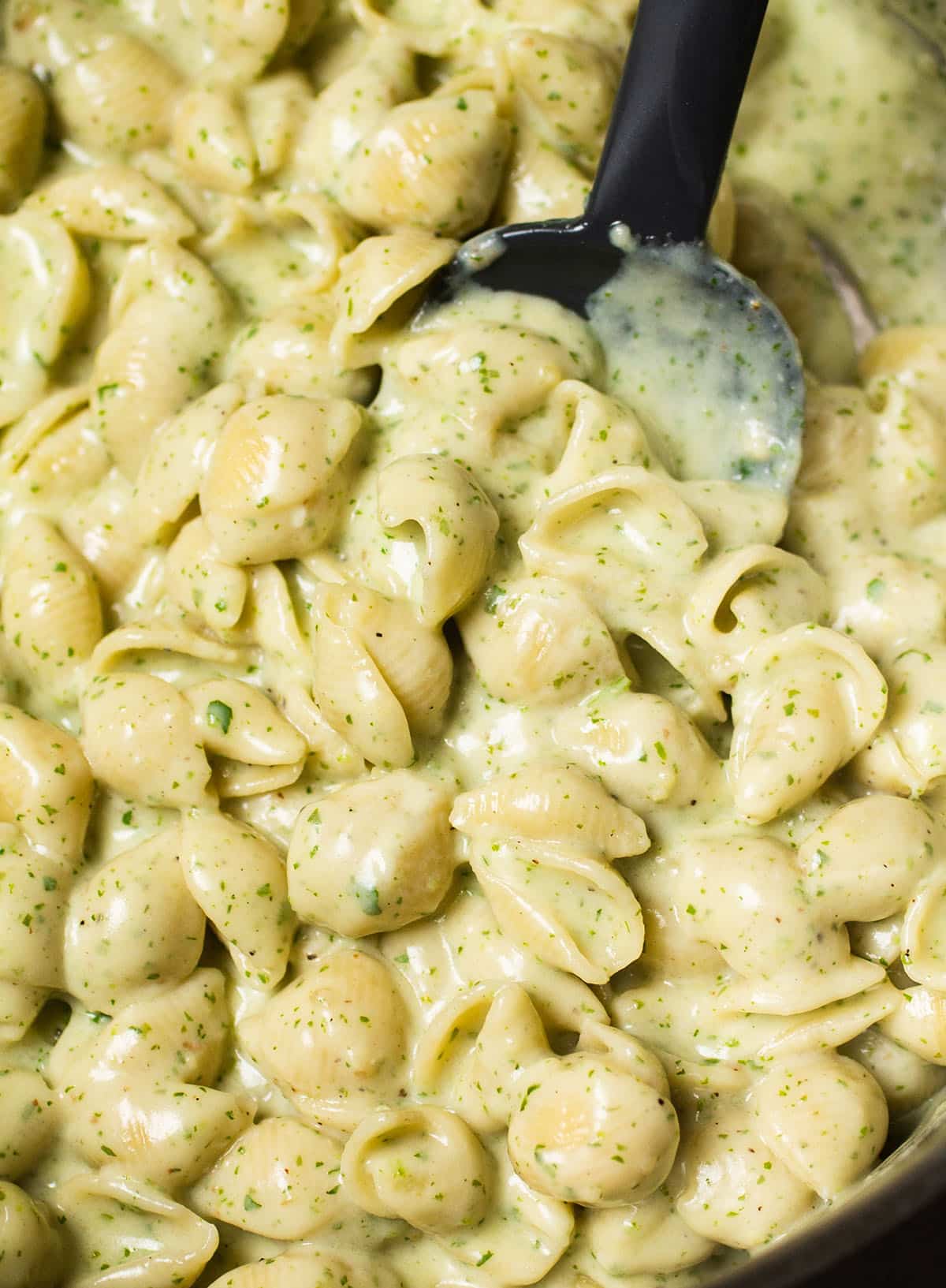 Black spoon stirring shell pasta into arugula white cheddar cheese sauce.