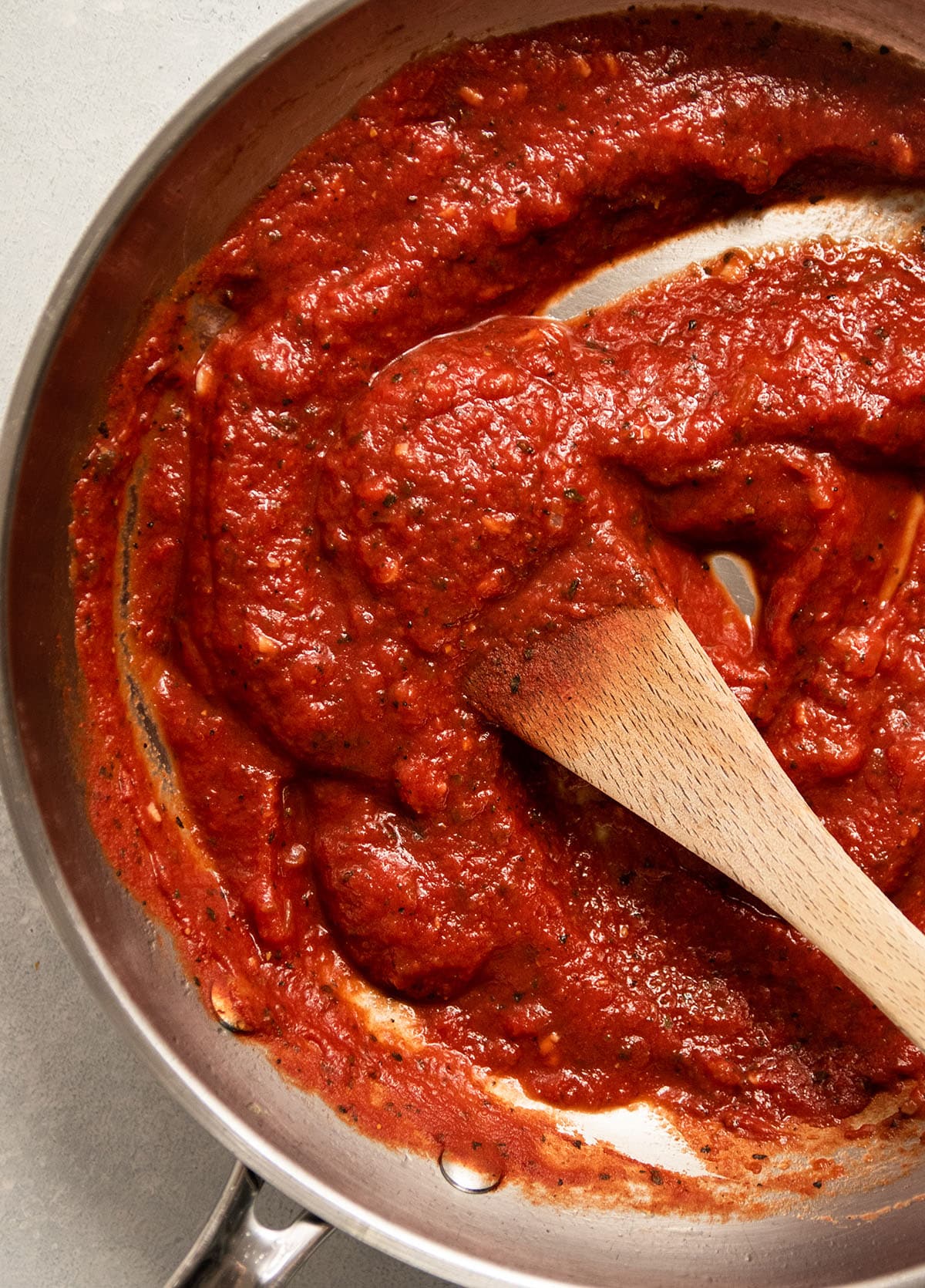 Wooden spoon stirring thickened pizza sauce in a silver skillet.