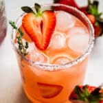 Strawberry cocktail garnished with a fresh strawberry, on a white table.