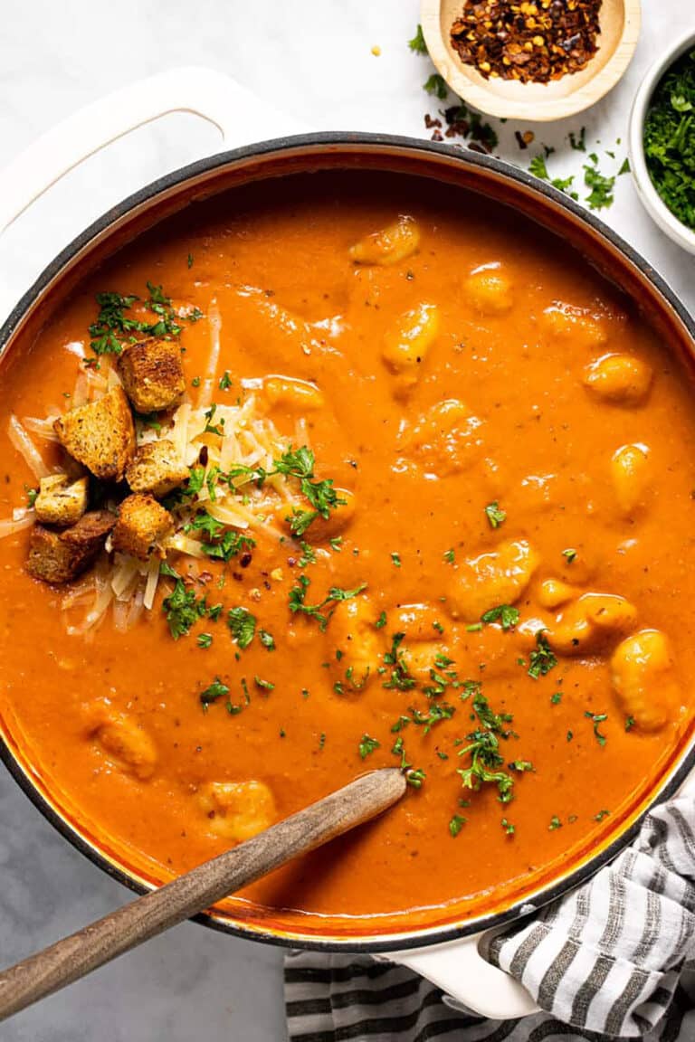 Tomato gnocchi soup in a large pot with a wooden spoon.