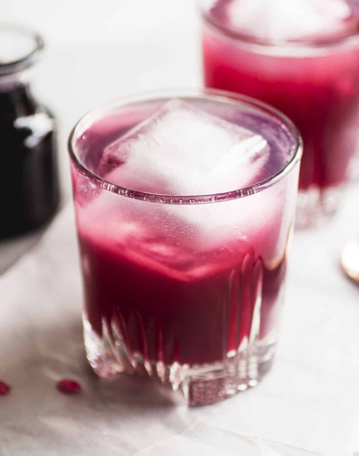 Bright pink whiskey spritzer in a short glass with a large ice cube.