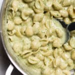 Arugula mac and cheese in a large silver pot with a black spoon.